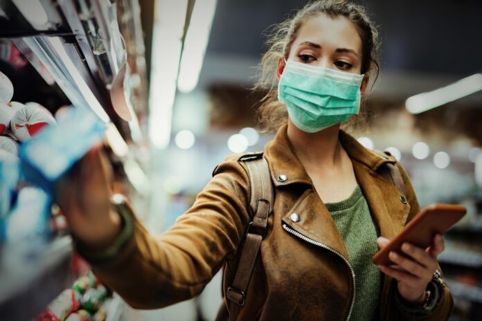 Young,Woman,With,Face,Mask,Using,Mobile,Phone,And,Buying