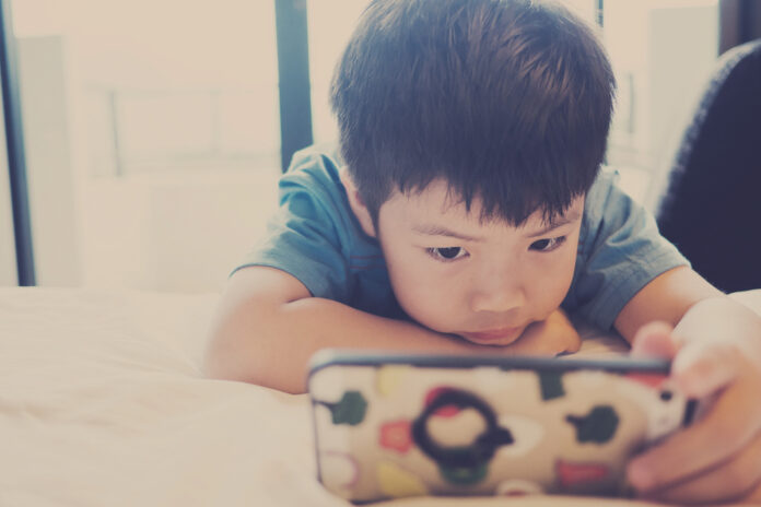 Asian,Chinese,Boy,Playing,Smartphone,On,Bed.,Watching,Smartphone.,Kid