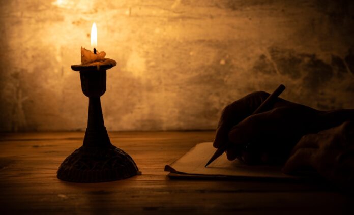 Hand,Writing,Letter,With,Pencil,On,Paper,In,Candle,Light